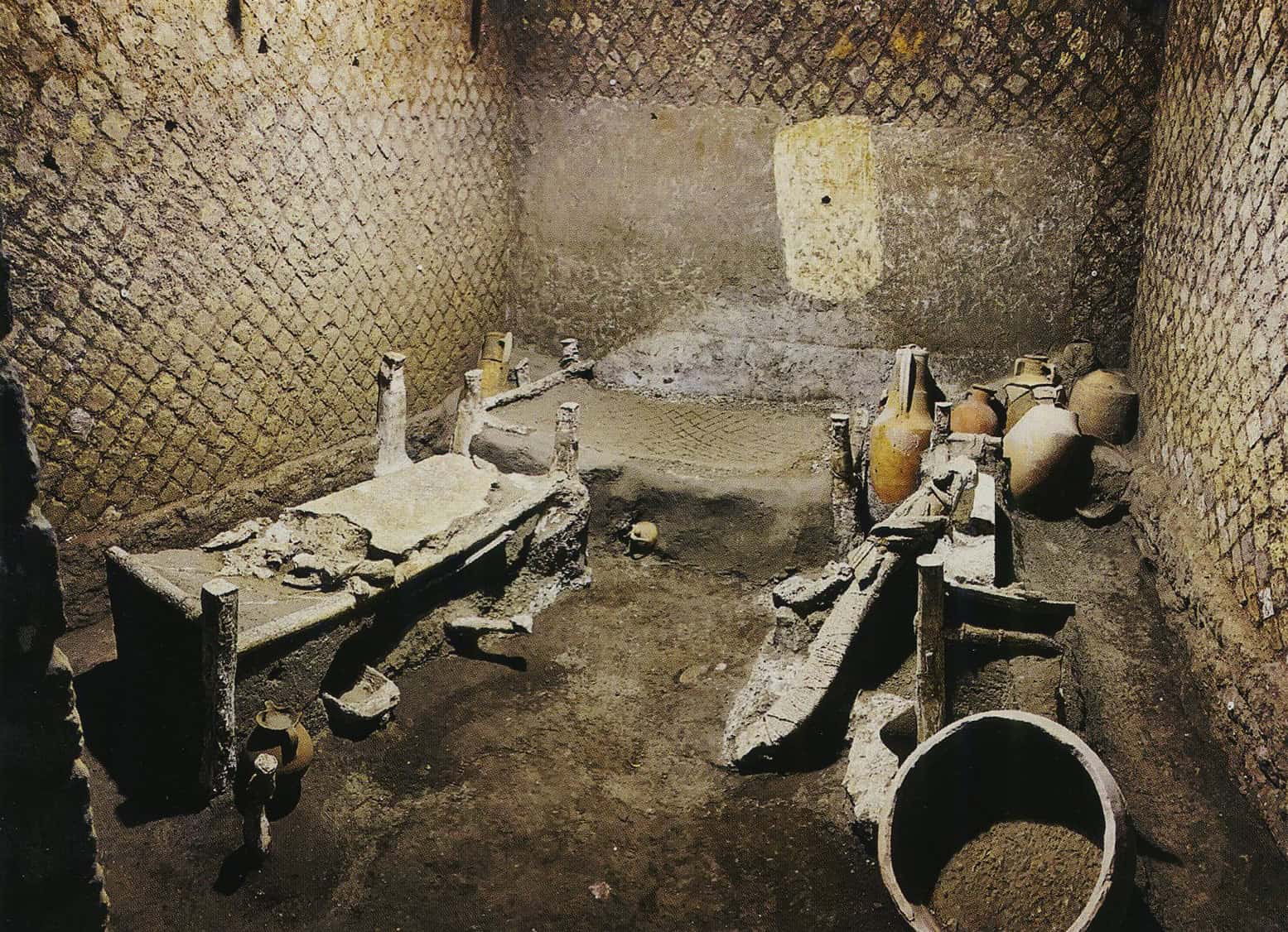 Valokuva pienestä huoneesta, jossa on neljä vuodetta. Takaseinällä on valkoiseksi maalattu suorakaide. Nurkassa on ruukkuja.