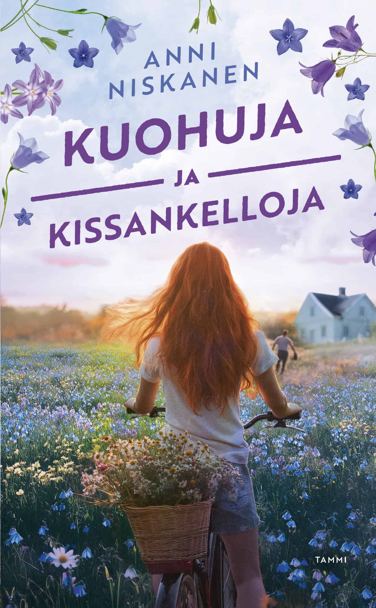 Naisen pyörän tarakalla on kukkakori. Hän kulkee kukkaniityllä kohti kaksikerroksista taloa edellään mies.