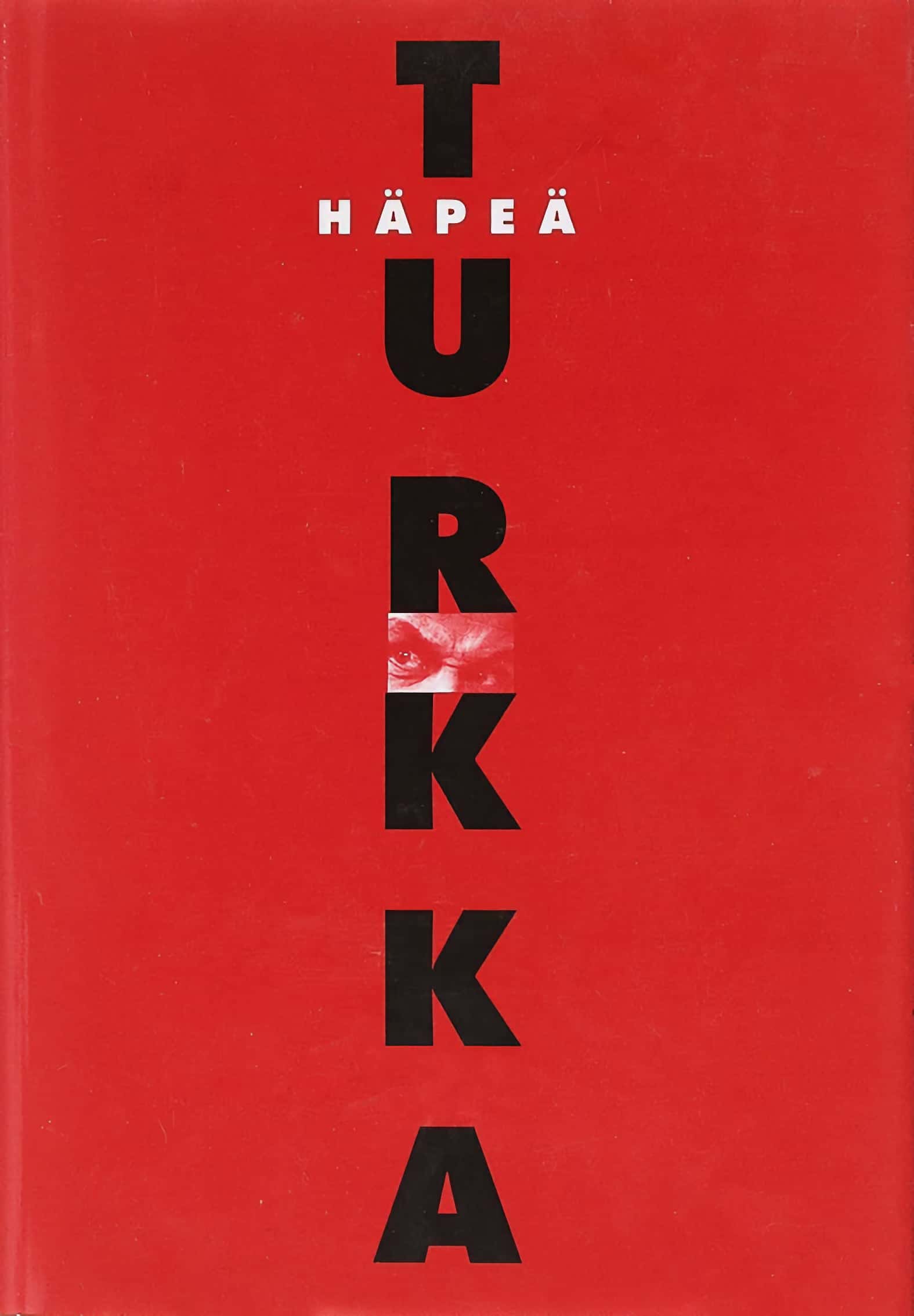 Häpeä-romaanin punaisessa kannessa lukee TURKKA isoin mustin kirjaimin. Kannen keskellä on pieni kuva tuijottavista silmistä.