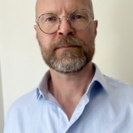 Valokuva Sami Montellista. Kuvassa on kaljupäinen, parrakas mies, jolla silmälasit ja vaaleansininen kauluspaita.